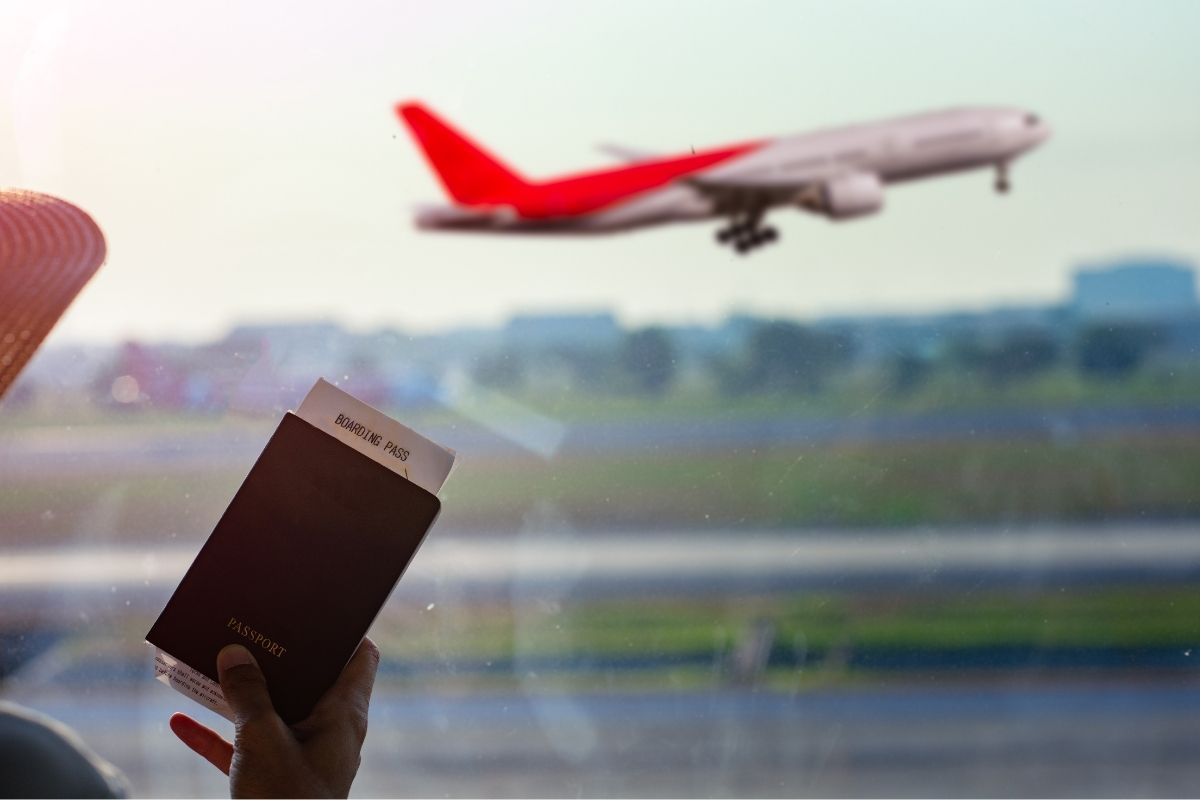 Hand holding a passport and boarding pass with a red airplane taking off in the background.